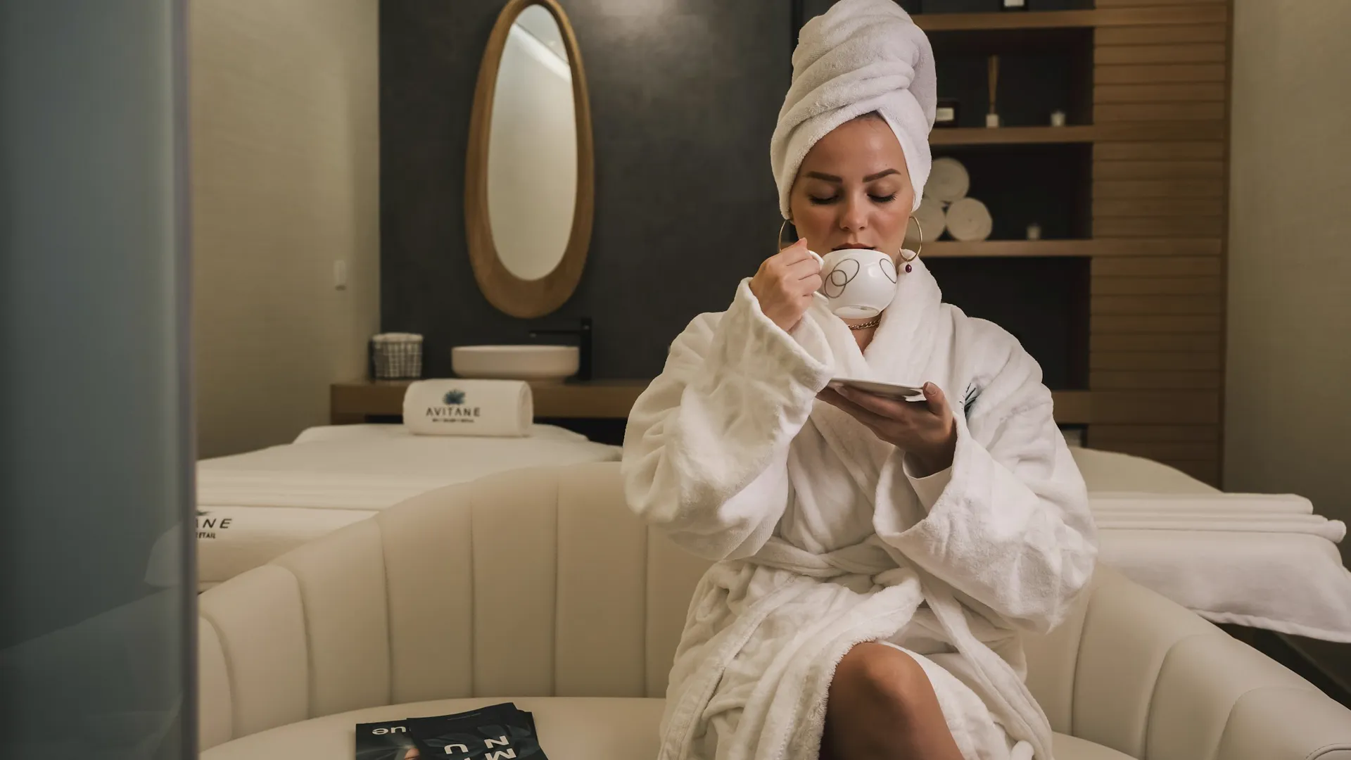 Salon de repos du centre : fauteuils clairs, lumière douce, une cliente en peignoir