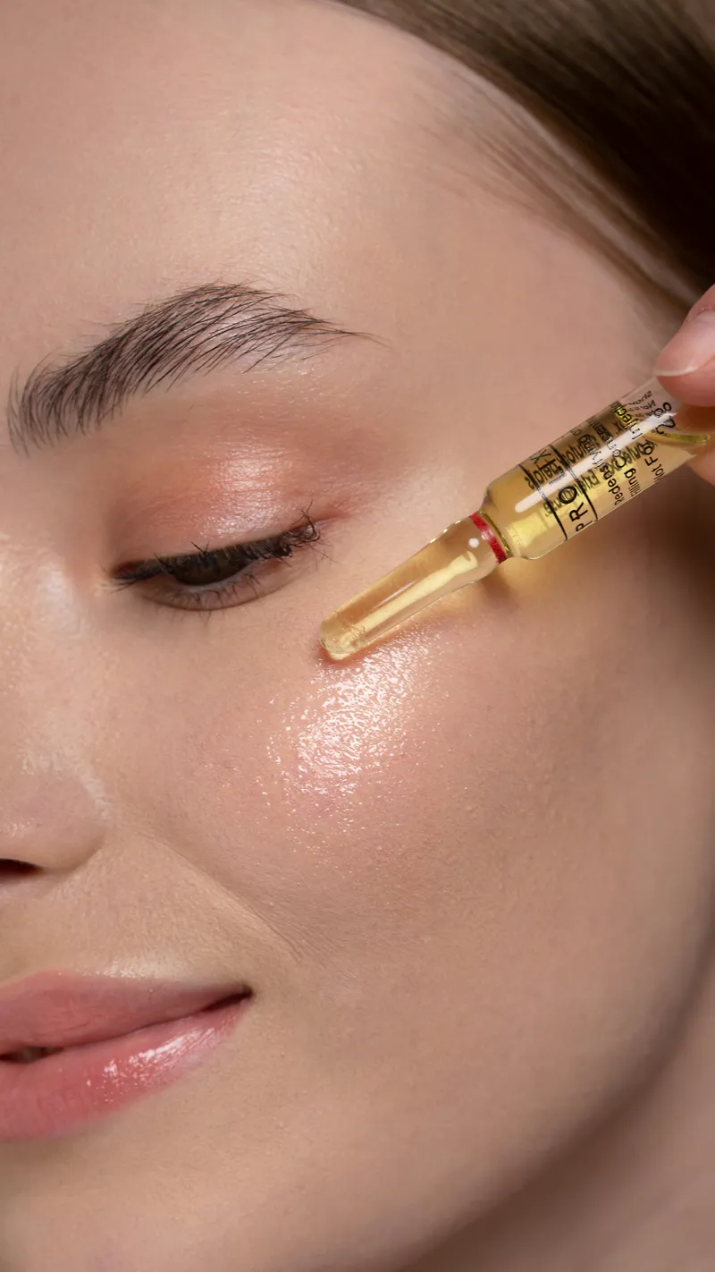 Une ampoule de soin dorée appliquée sur une peau nette et lumineuse